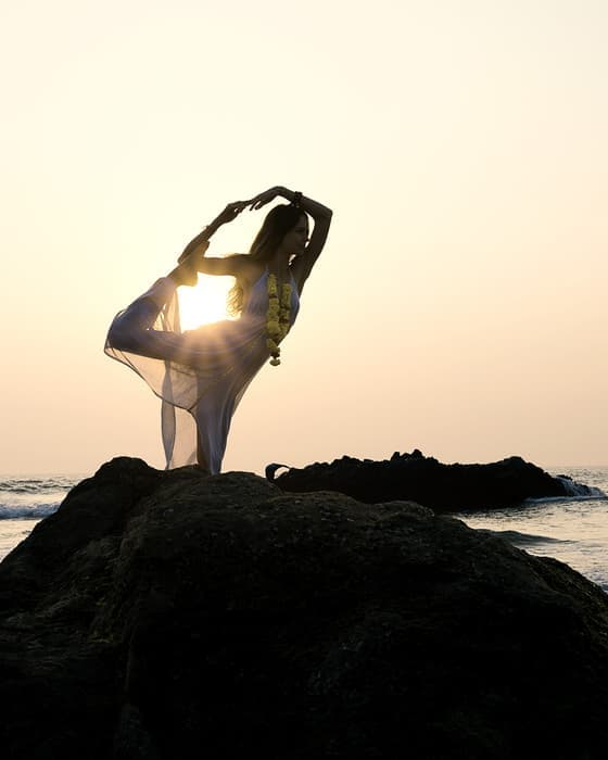 Silhouette in dancer pose on a rock as the sun sets behind