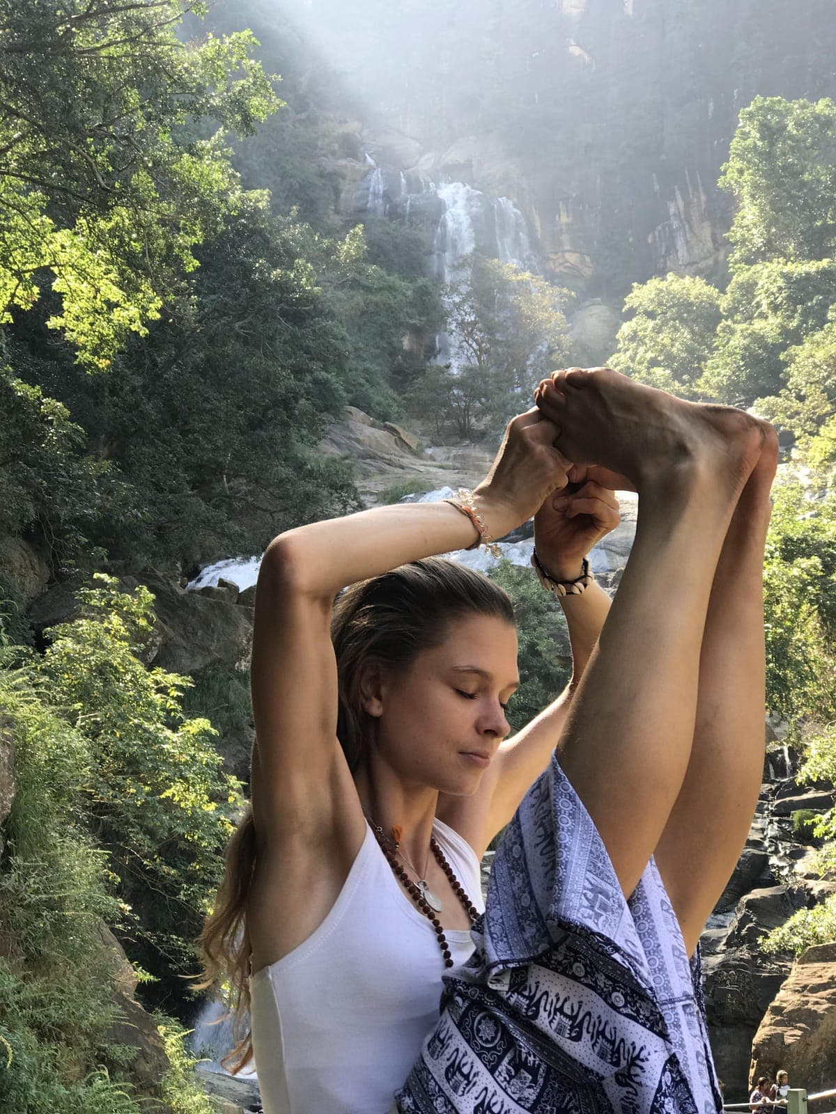 Arms bound overhead in front of a jungle waterfall